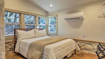 Een slaapkamer met een bed, grote ramen, een stenen muur en een airconditioner.