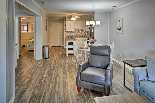 Un espacio habitable compacto con comedor, cocina y zona de estar con una silla de cuero gris y una pequeña mesa.