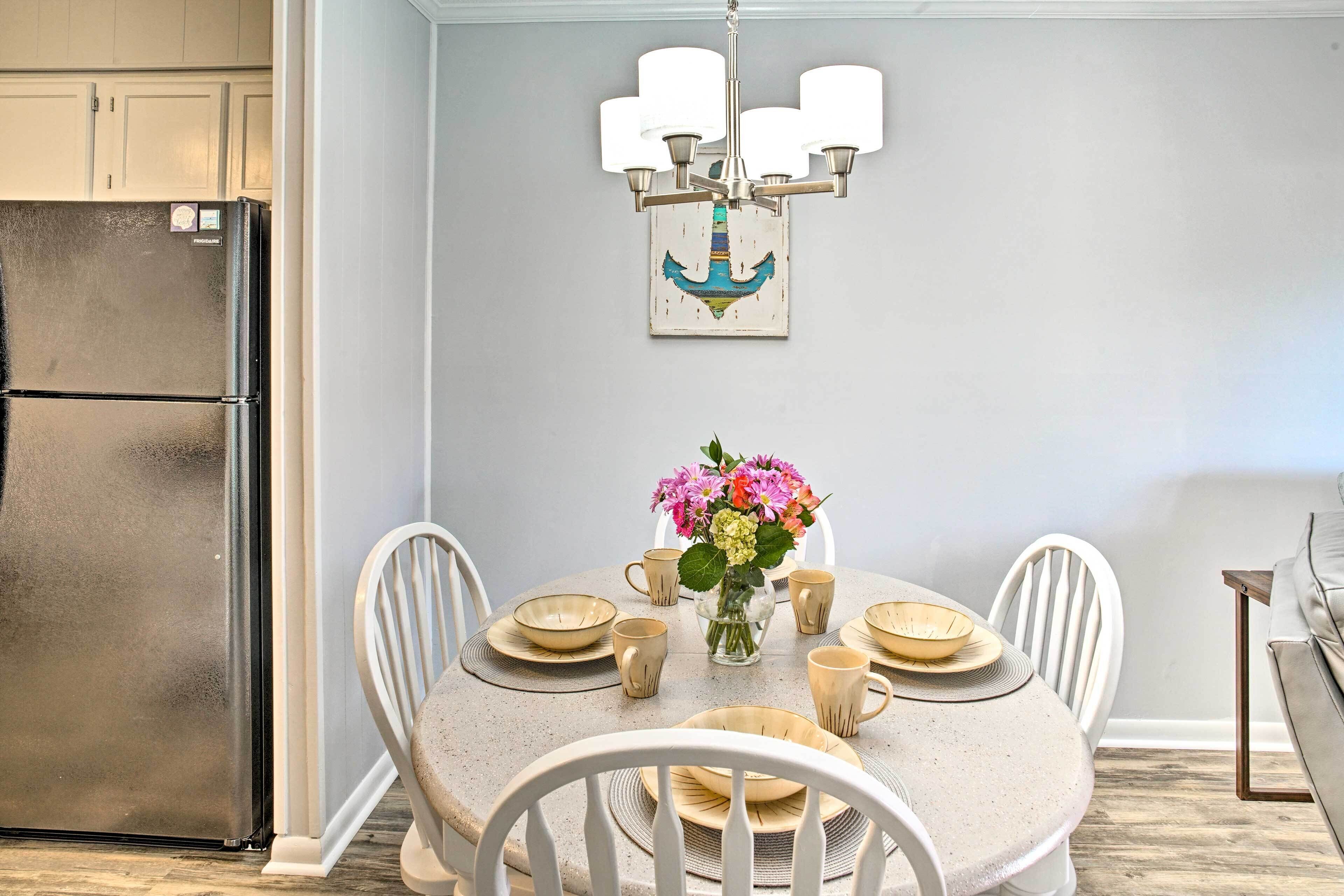 A dining area with a round table set for six, surrounded by white chairs. A chandelier with multiple lights hangs above the table.