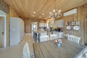 Una cocina amplia con paredes de madera, una isla central, armarios blancos y un comedor con mesa y sillas de madera.