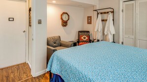 Een slaapkamer met een bed, een stoel, een kapstok en een klok aan de muur.