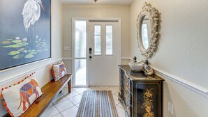 A hallway with a bench, a framed painting, a mirror, and a door.