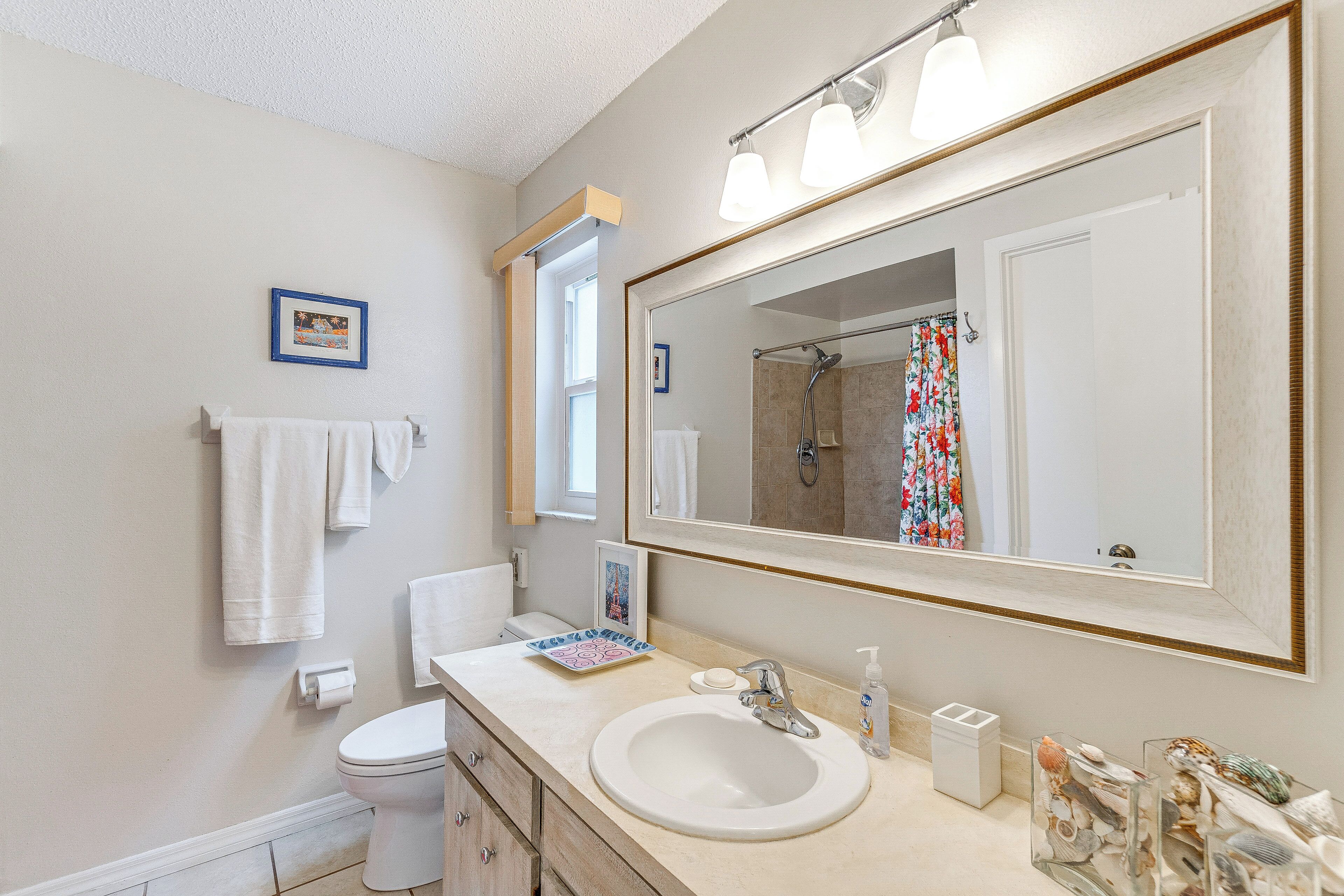 A bathroom with a large mirror, a sink, a toilet, and a shower.