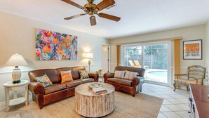 A living room with two leather sofas, a round coffee table, a ceiling fan, and a large window.