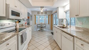 A kitchen with white cabinets, a granite countertop, a dining table with chairs, and a window with a view of trees.