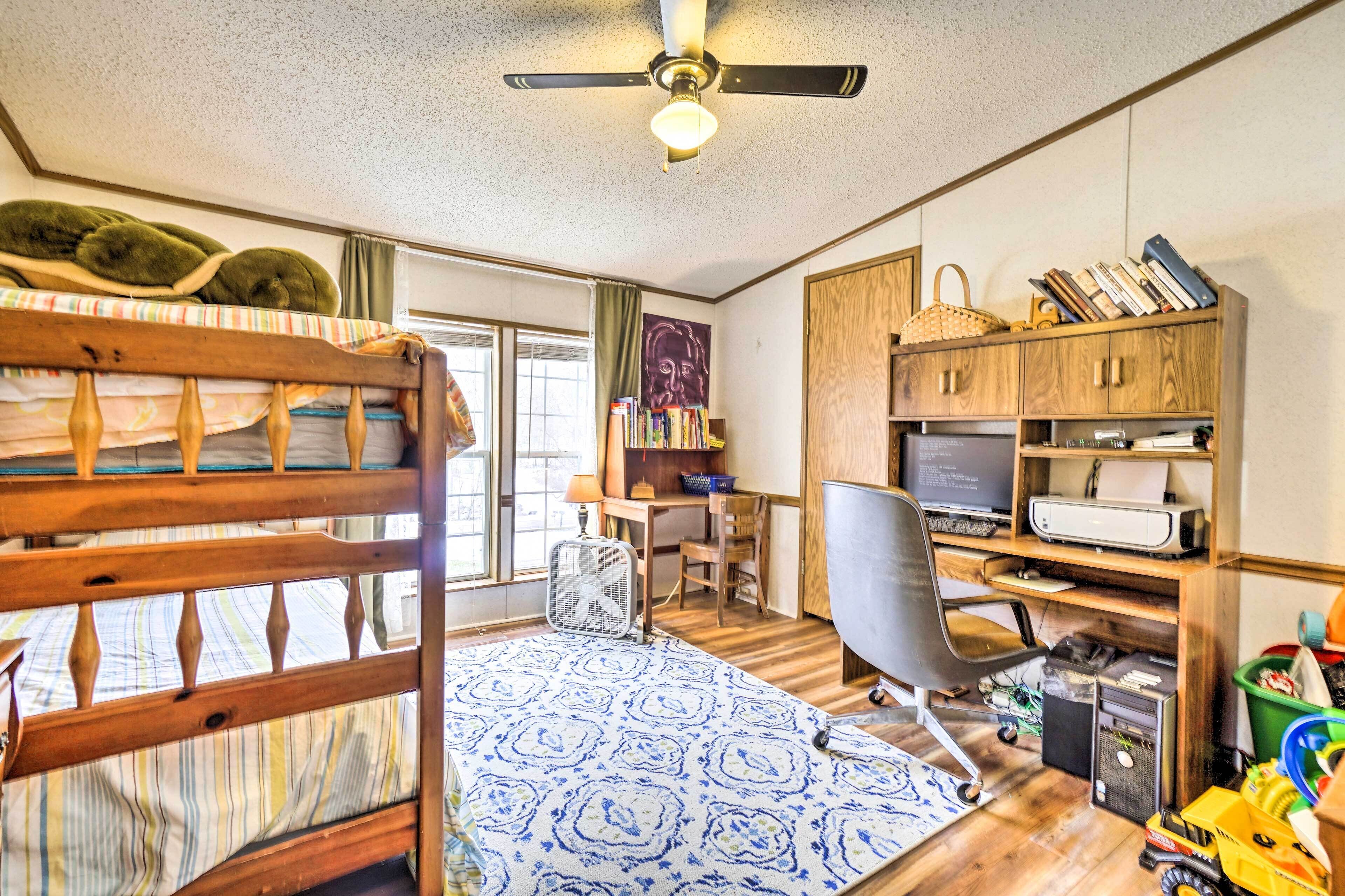 A room with a bunk bed, desk, chair, computer, printer, and shelves with books and a basket.