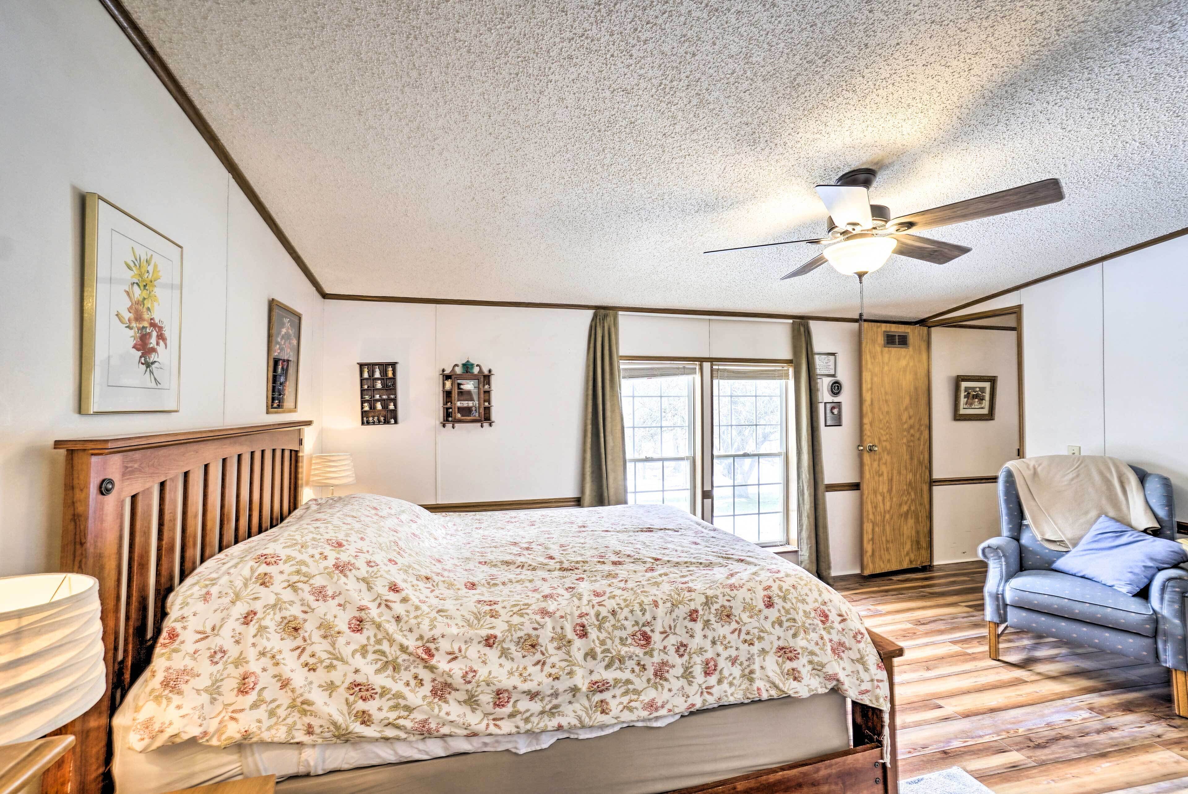 A bedroom with a wooden bed, a ceiling fan, a chair, and a window.