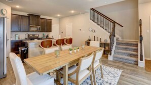 Une cuisine moderne avec des meubles en bois foncé, un four à micro-ondes en acier inoxydable et un coin repas comprenant une table en bois et des chaises blanches.