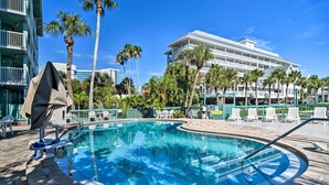 Une piscine à l’eau d’un bleu cristallin, entourée de palmiers et, au fond, un bâtiment doté de nombreux balcons.