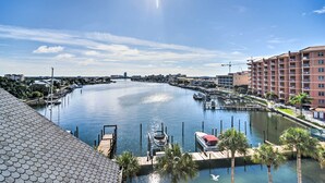 Un port de plaisance avec des bateaux amarrés, un ciel dégagé et un immeuble à plusieurs étages en arrière-plan.