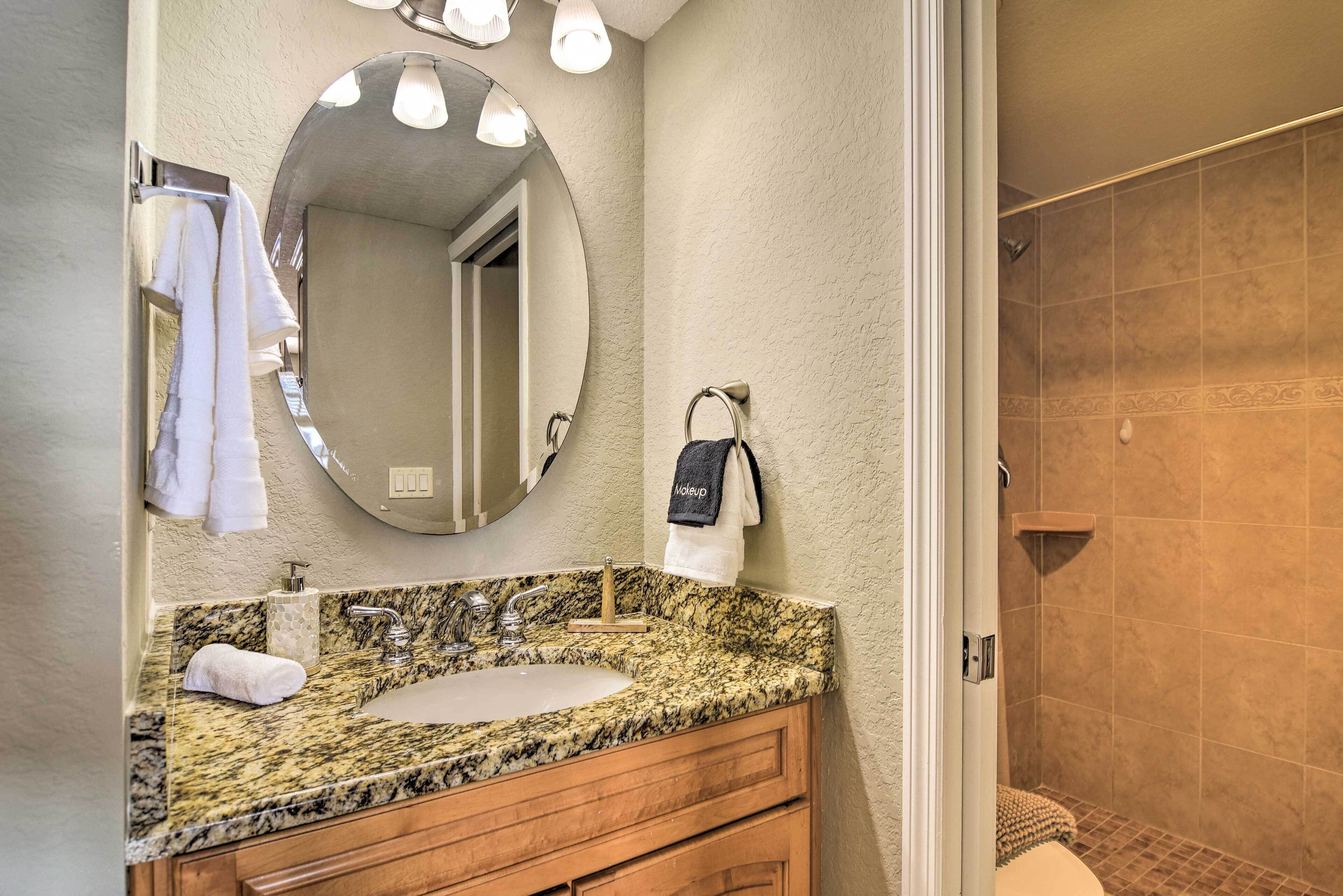 A bathroom with a granite countertop sink, a mirror, and a shower area.