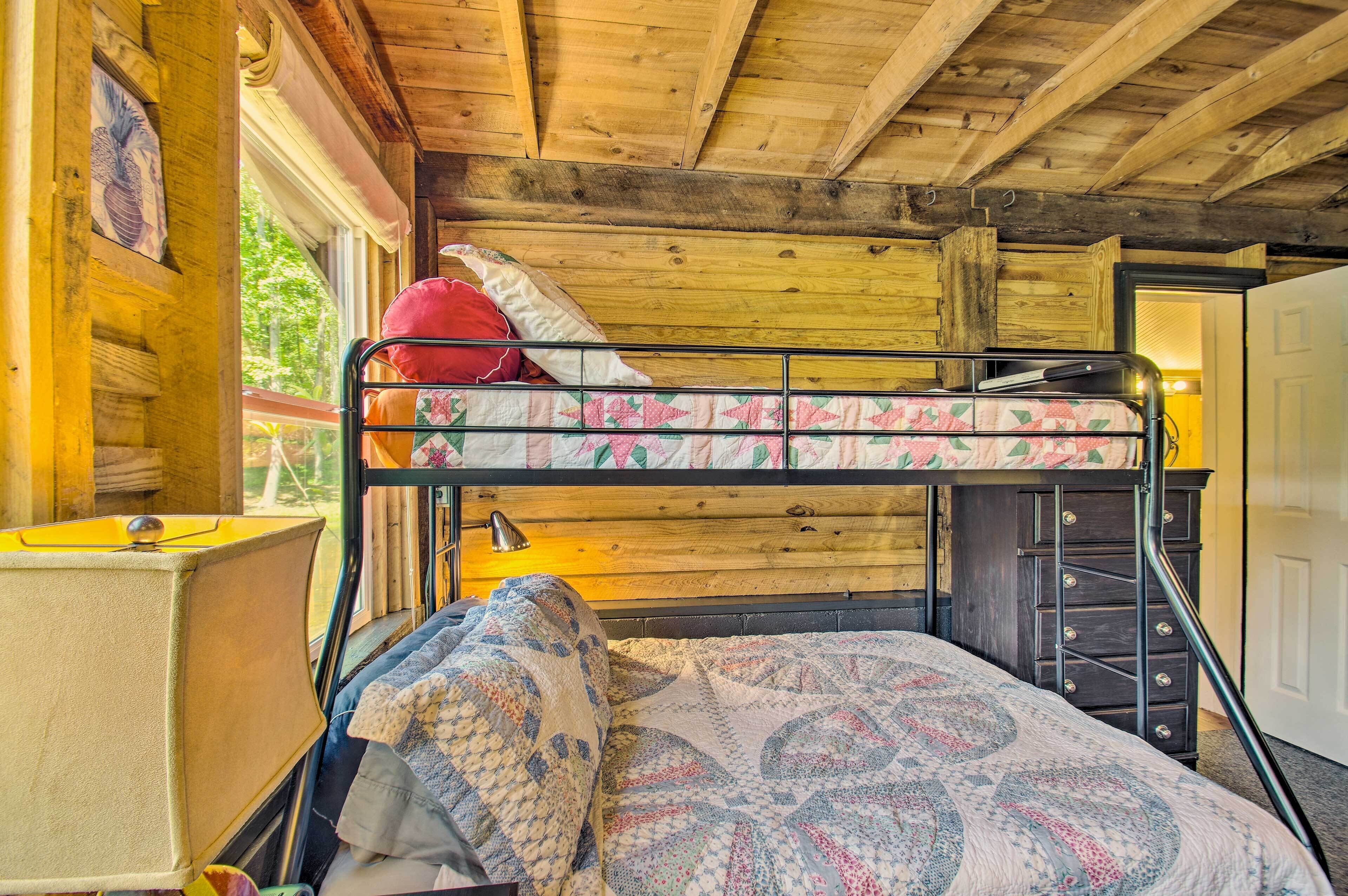 A bunk bed with a patterned quilt, a lamp, and a dresser in a cabin-style room with wooden walls and a window.