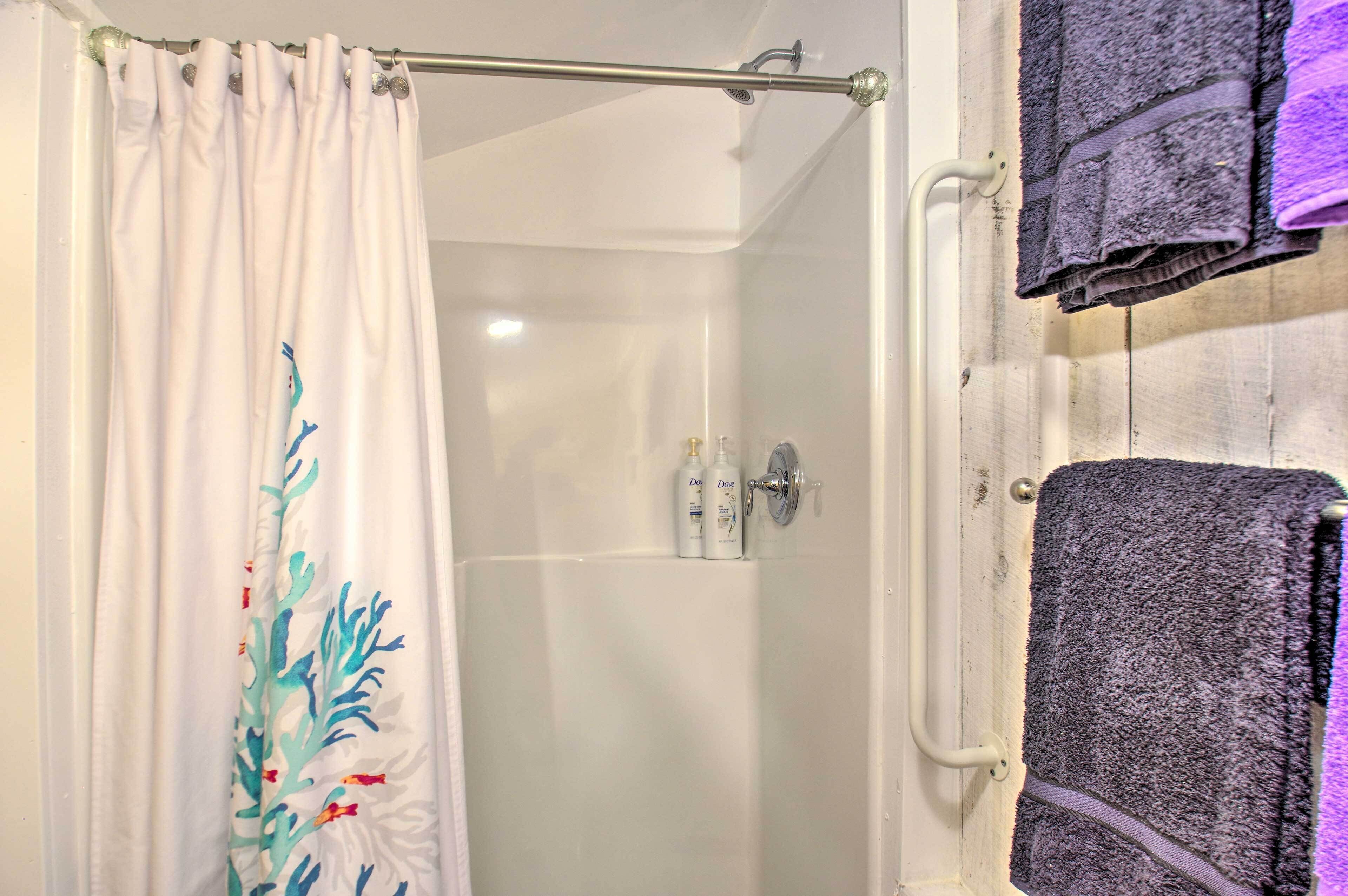 A bathroom with a shower curtain, a towel rack with towels, and toiletries on the wall.