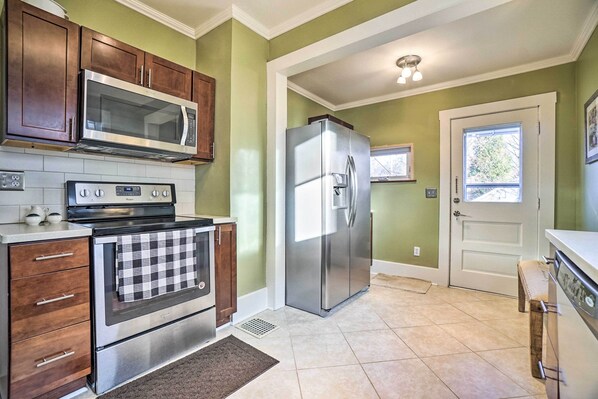 A kitchen with a stainless steel refrigerator, a microwave, and an oven. There is a window with a view of trees outside. - Charming & Family-friendly Zanesville Home! (Zanesville)