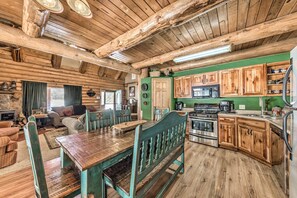 A rustic cabin interior with a wooden dining table, benches, a kitchen with wooden cabinets, and a fireplace. - Cozy Alto Cabin on 2 Acres: Near Fishing & Skiing! (Alto)