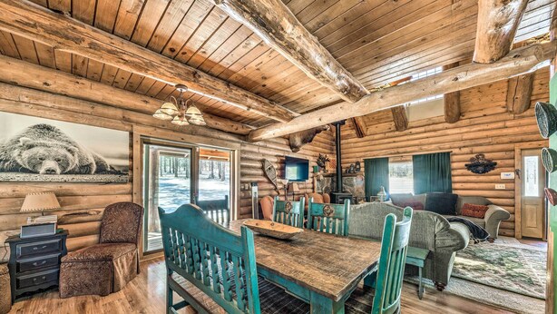 A rustic log cabin interior with a wooden dining table, chairs, a sofa, and a television. - Cozy Alto Cabin on 2 Acres: Near Fishing & Skiing! (Alto)