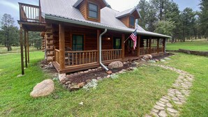 A log cabin with a porch, a covered deck, and an American flag. - Cozy Alto Cabin on 2 Acres: Near Fishing & Skiing! (Alto)