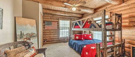 A log cabin interior with a bunk bed, a ceiling fan, and a painting of a moose.