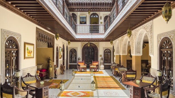 Un interior tradicional con un espacio central abierto, muebles de madera ornamentados y alfombras estampadas.
