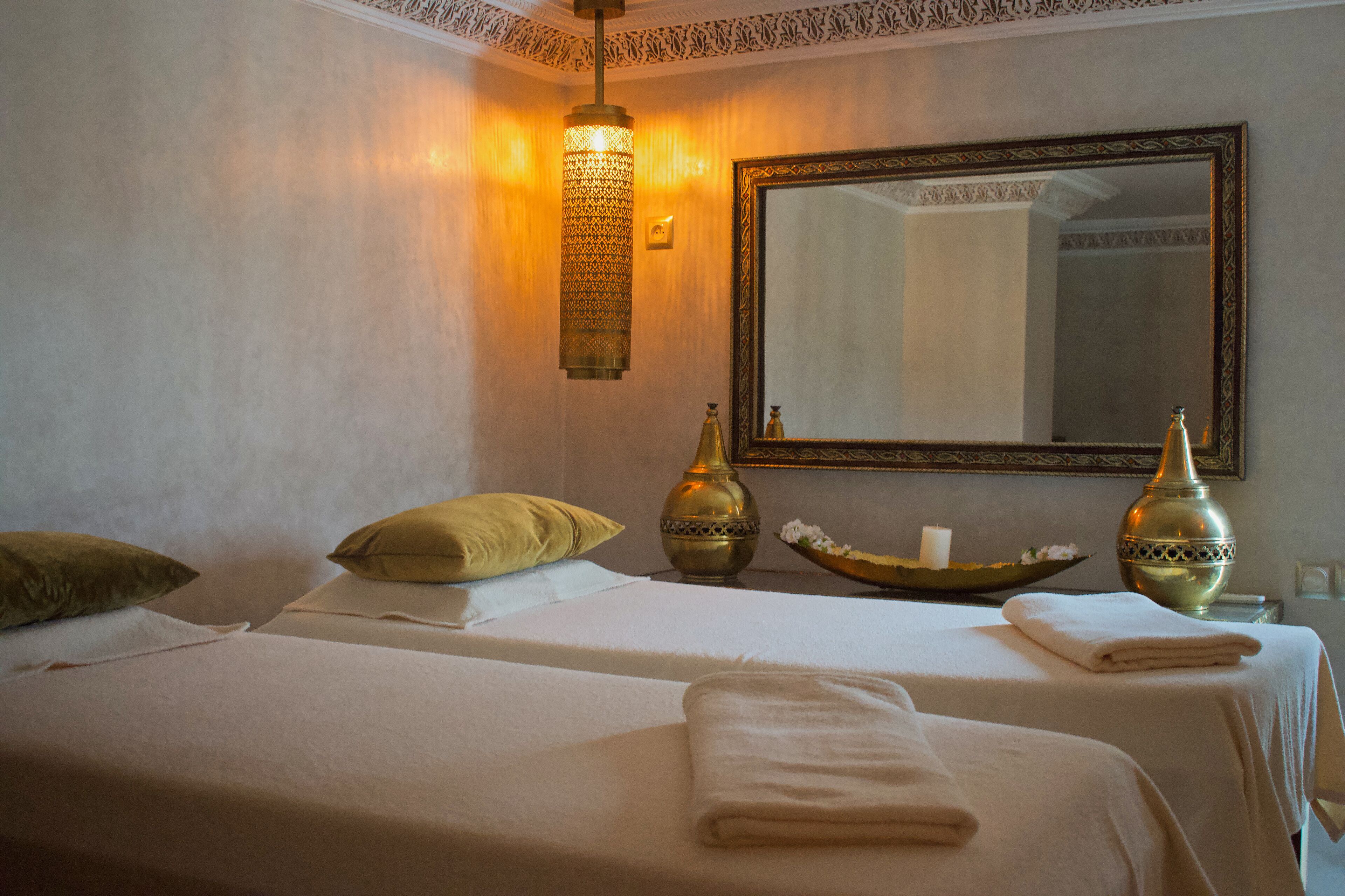 A hotel room with two beds, a large mirror, decorative vases, and a wall-mounted light fixture.