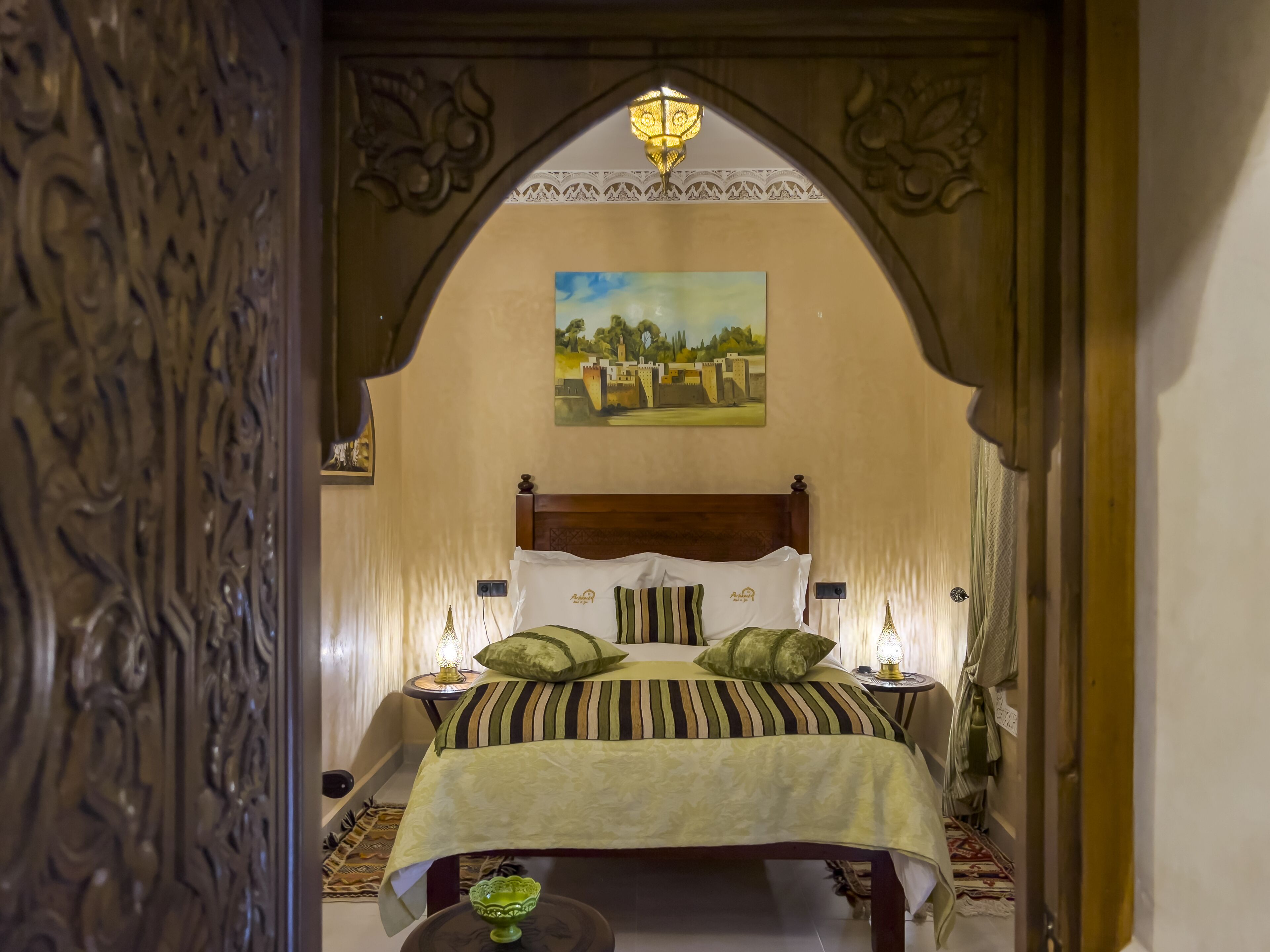 Una habitación con una cama, dos mesitas de noche, un cuadro en la pared y una lámpara decorativa en el techo.
