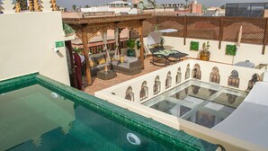 Un área de piscina en la azotea con una sección acristalada, mobiliario exterior y una pérgola.