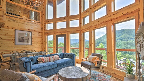 A spacious wooden cabin with large windows offering mountain views, a blue sofa, and a dining area. - Mountain Dew Cabin w/ Hot Tub & Scenic Views! (Sevierville)
