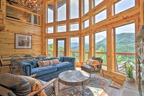 Une cabane en bois spacieuse, dotée de grandes fenêtres offrant une vue sur les montagnes, d’un canapé bleu et d’un coin repas.