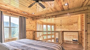 A wooden cabin bedroom with a large bed, a ceiling fan, and a view of a wooden deck through a window. - Mountain Dew Cabin w/ Hot Tub & Scenic Views! (Sevierville)