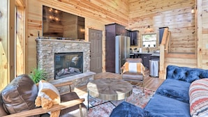 A cozy cabin interior with a stone fireplace, wooden walls, a sofa, and a dining area. - Mountain Dew Cabin w/ Hot Tub & Scenic Views! (Sevierville)