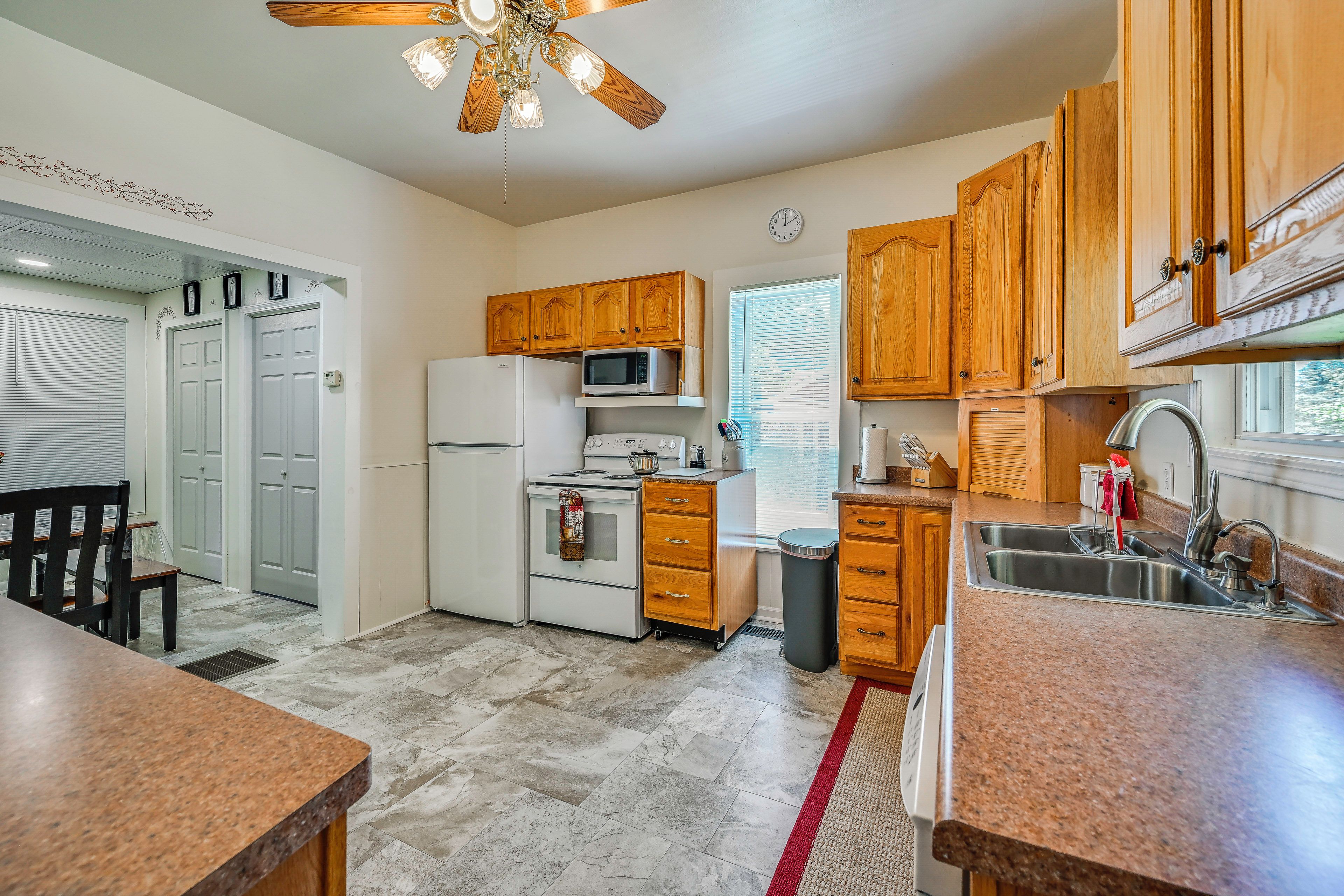 A kitchen with wooden cabinets, a microwave, a stove, a sink, and a ceiling fan.