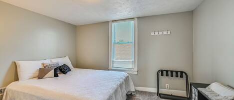 Un dormitorio con cama, ventana con persianas, lámpara de pared y un estante metálico negro.
