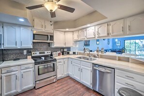 A modern kitchen with white cabinets, stainless steel appliances, and a large window offering a view of the outdoors.