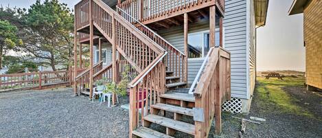 A wooden staircase leading to a deck with a railing, a gravel driveway, and a picnic table in the background.