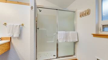 A bathroom with a glass shower enclosure, wooden vanity, and white towels.