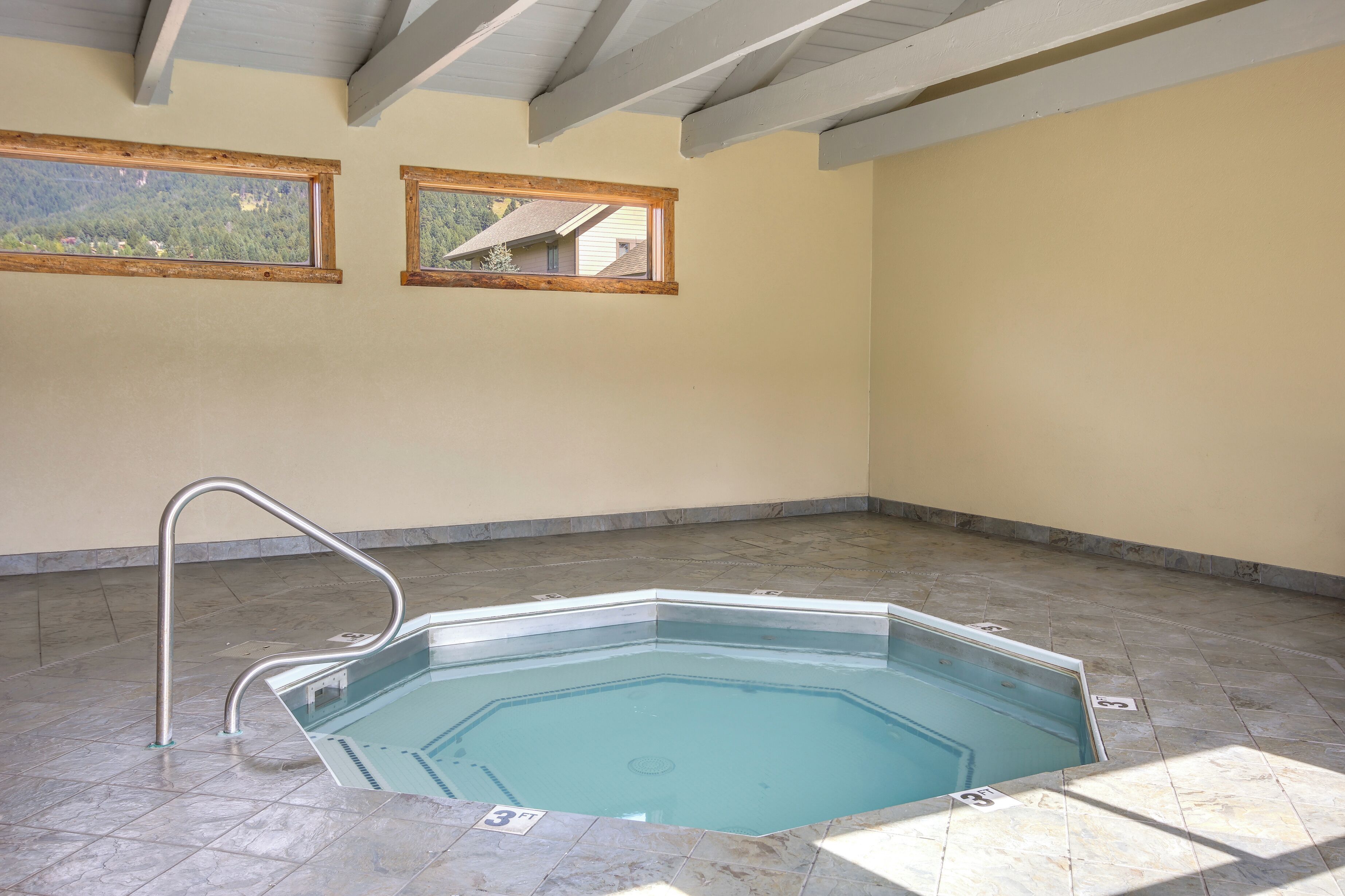 A swimming pool with a metal ladder, tiled floor, and two windows with wooden frames.