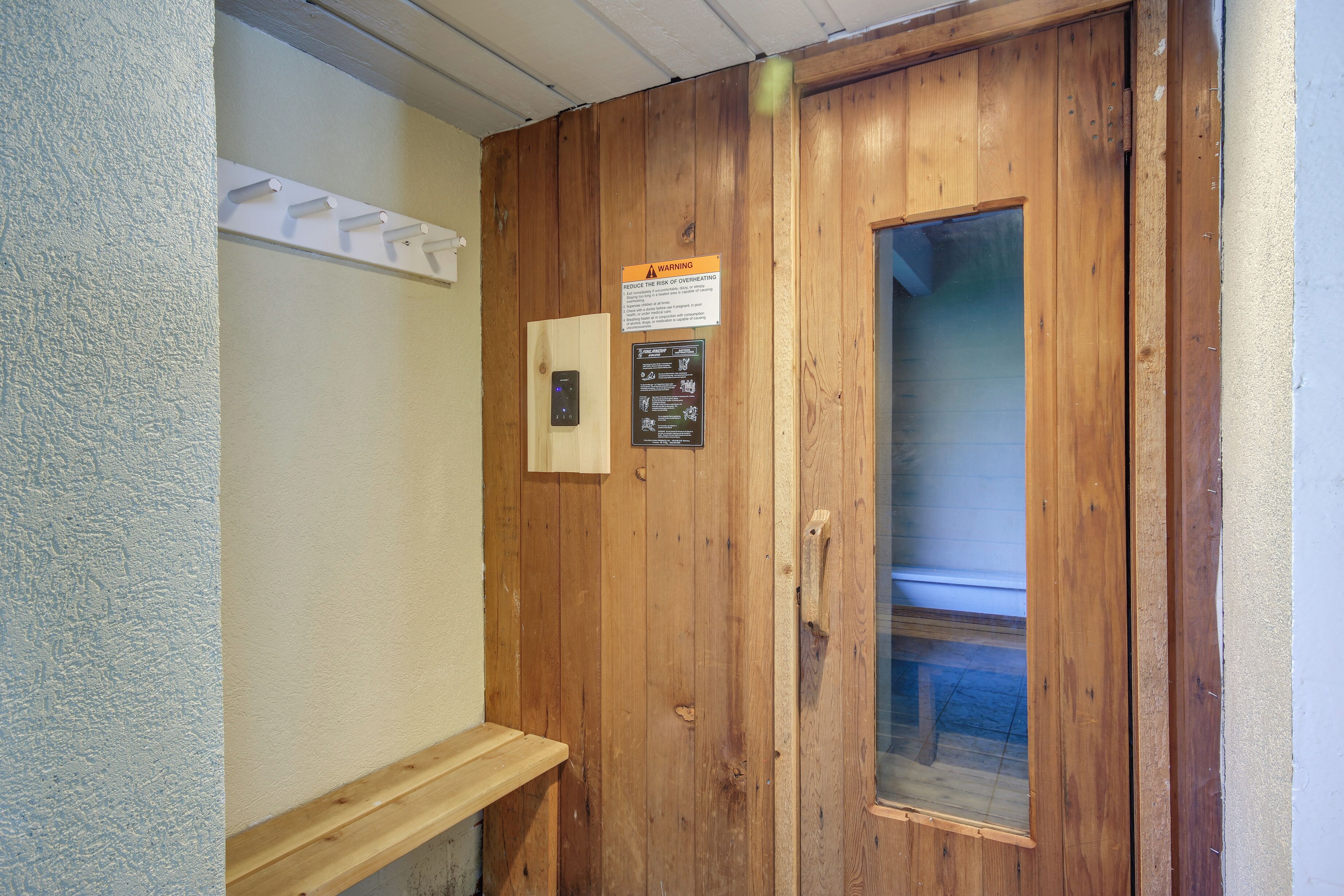 A wooden door with a window, a warning sign, and a light switch on the wall.