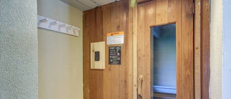 A wooden door with a window, a warning sign, and a light switch on the wall.
