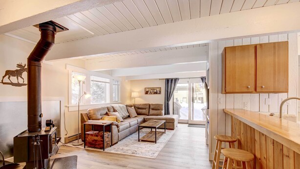A cozy living room with a fireplace, a sofa, a coffee table, and a wooden bar with stools. - Cozy Condo Near Golf, 7 Mi to Big Sky Resort! (Big Sky)