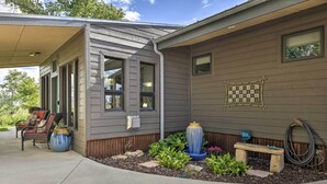 Une maison d’habitation dotée d’un porche abrité, d’un espace extérieur aménagé avec des sièges et d’un jardin agrémenté de plantes et d’un abreuvoir pour oiseaux.