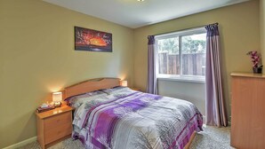A bedroom with a bed, bedside table, lamp, window with curtains, and a painting on the wall. - Waterfront Discovery Bay Home: Outdoor Bar & Dock (Discovery Bay)