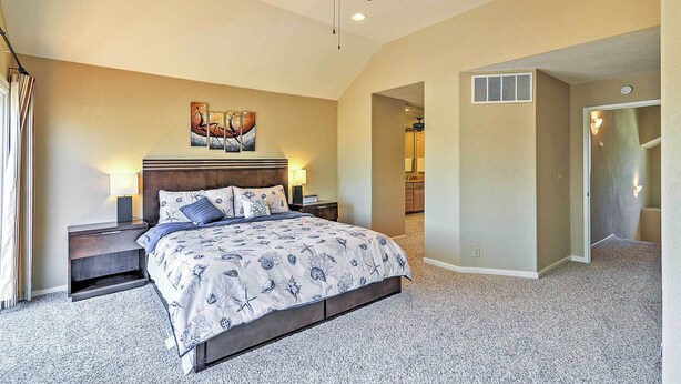 A bedroom with a bed, nightstands, a ceiling fan, a painting, and a hallway leading to a bathroom. - Waterfront Discovery Bay Home: Outdoor Bar & Dock (Discovery Bay)