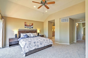 A bedroom with a bed, nightstands, a ceiling fan, a painting, and a hallway leading to a bathroom.