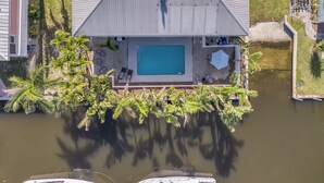 An aerial view of a house with a swimming pool, surrounded by palm trees and a small dock. - Bokeelia Island Oasis: Waterfront, Private Dock! (Bokeelia)