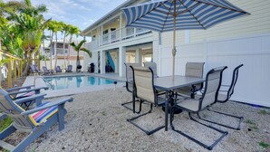 A poolside area with a table and chairs, a striped umbrella, and lounge chairs. - Bokeelia Island Oasis: Waterfront, Private Dock! (Bokeelia)