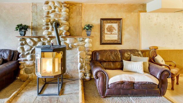 A cozy living room with a stone wall, a fireplace, leather sofas, and a framed picture on the wall. - Main Street Townhome - 12 Miles to Bear Lake! (Paris)
