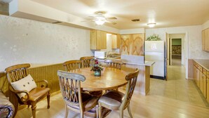 A dining area with a round wooden table surrounded by six chairs, a ceiling fan, and a kitchen in the background. - Main Street Townhome - 12 Miles to Bear Lake! (Paris)