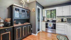 A modern kitchen with dark cabinetry, a built-in oven, and a window overlooking greenery. - Hot Tub, Fire Pit & Barrel Sauna: Poconos Abode (Long Pond)