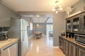 A modern kitchen with stainless steel appliances, a dining area with a wooden table, and a view of the outdoors through a large window. - Hot Tub, Fire Pit & Barrel Sauna: Poconos Abode (Long Pond)