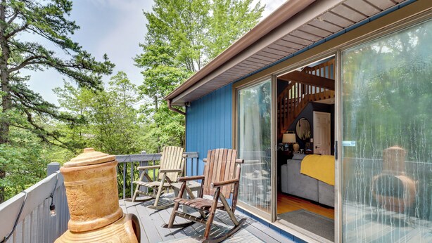 A deck with rocking chairs and a large vase, overlooking a forested area. - Hot Tub, Fire Pit & Barrel Sauna: Poconos Abode (Long Pond)